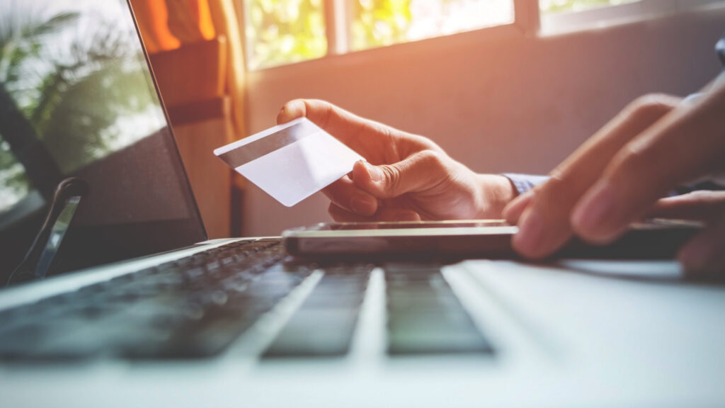 Man holding credit card in hand and entering security code using smart phone on laptop keyboard, online shopping concept.